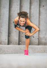 Happy fitness young woman stretching outdoors in the city