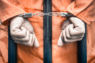 Handcuffed hands of a prisoner behind the bars of a prison