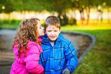 Little boy and girl whispers in autumn park.