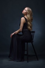 Obraz na płótnie Canvas Beautiful woman in a black evening dress posing with chair