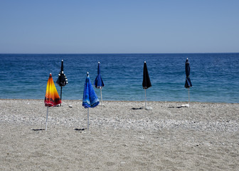 closed beach umbrellas on an empty stony beach on a sunny day