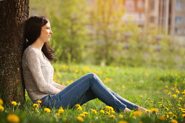 The lonely girl sits at a tree looks in a distance