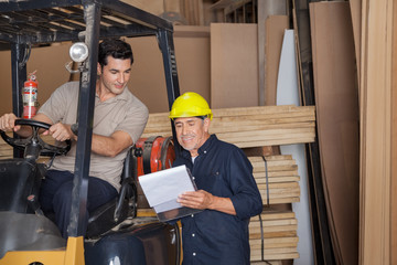 Carpenter Holding Clipboard By Colleague In Forklift