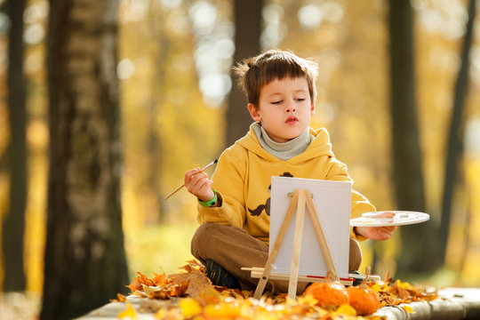 Cute little boy painting in golden autumn park