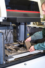 Worker examining metal detail in cnc industrial machine