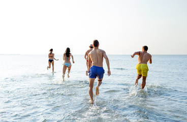 smiling friends running on beach from back
