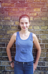 Fototapeta na wymiar portrait of a smiling teenager girl leaning against a brick wall
