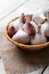 Fresh garlic in wicker basket, on wooden background