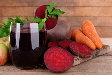Glass of fresh beet juice and vegetables on wooden background