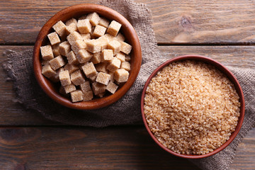Brown sugar cubes and crystal sugar in bowl on wooden