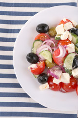 Greek salad served in plate on napkin on fabric background