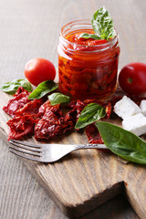 Sun dried tomatoes in glass jar, basil leaves and feta cheese