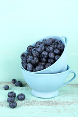 Tasty ripe blueberries in cups, on wooden table