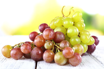 Bunches of ripe grapes on wooden table on natural background