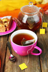 Cup with tea, teapot and tea bags on wooden table close-up