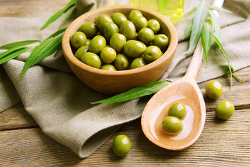 Green olives in bowl with leaves on table close-up