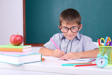 Schoolboy sitting in classroom on blackboard background