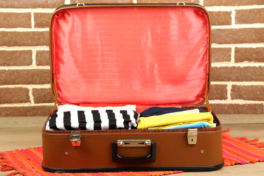 Female clothes in old suitcase on brick wall background