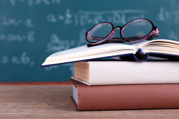 Books and glasses on wooden table on blackboard background