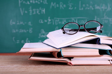 Books and glasses on wooden table on blackboard background