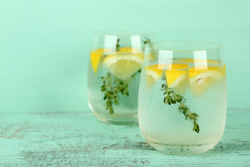 Tasty cool beverage with lemon and thyme, on wooden background