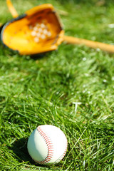 Baseball bat, ball and glove on green grass background