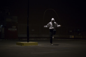 Hooded athlete skipping under a street light at night - obrazy, fototapety, plakaty