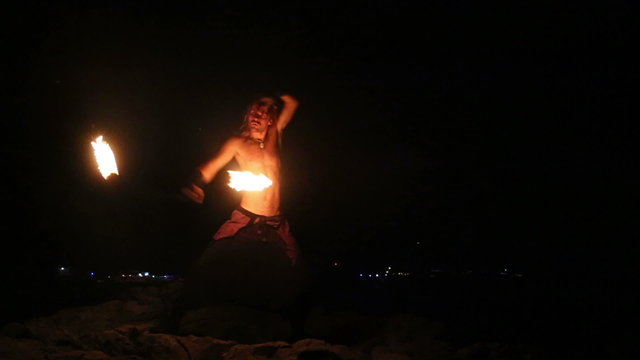 Male Artist of the spins fire poi on a rock 