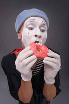 Portrait of handsome male mime eating a tasty pink donut with fu