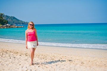 Fototapeta na wymiar Young woman in pink top and beige skirt walking on beach