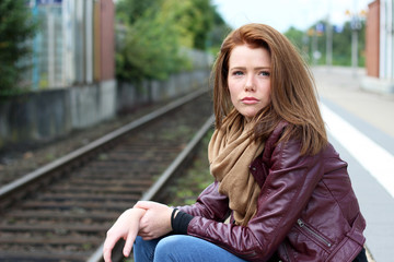 junge Frau sitzt traurig am Bahngleis