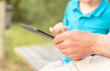 Grandfather hands using a tablet with granchild outdoors