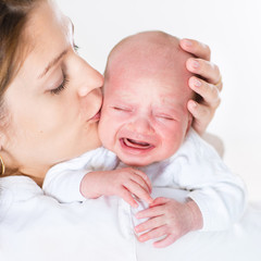 Young mother kissing her crying newborn baby