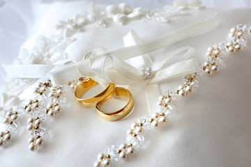 Gold wedding rings on a pillow with ribbons