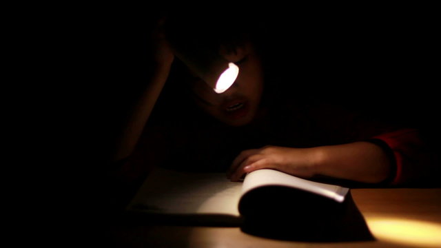HD Dolly: Asian girl reading book in darkness, with flashlig