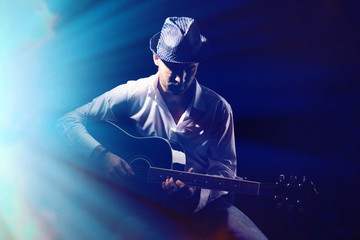Young musician playing acoustic guitar, on dark background