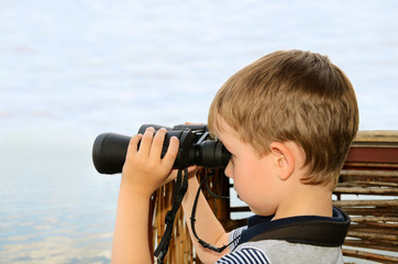 Obraz premium little boy looking through binoculars at sea. side view