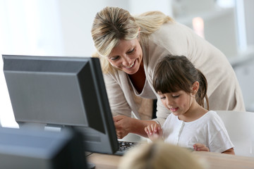 Teacher with little girl in class using computer and tablet