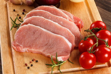 Raw pork chops on cutting board and vegetables