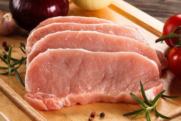Raw pork chops on cutting board and vegetables