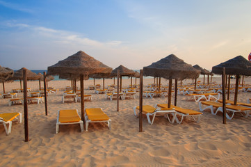 Umbrellas and deck lounges in the beach at sunset. Algarve