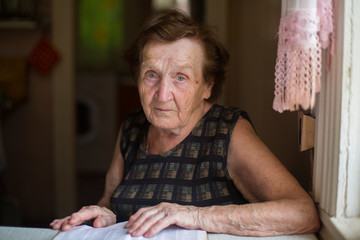 Worried elderly woman sitting at table in the house.
