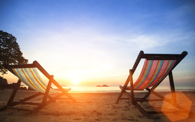 Pair beach loungers on the deserted coast sea at sunrise.