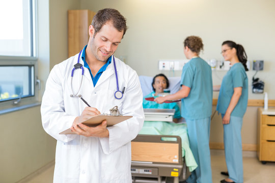 Doctor Writing On Clipboard With Nurses And Patient In Hospital