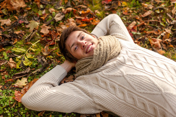 close up of smiling young man lying in autumn park