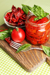 Sun dried tomatoes in glass jar, basil leaves