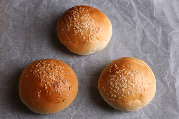 Tasty buns with sesame on oven-tray, on wooden background