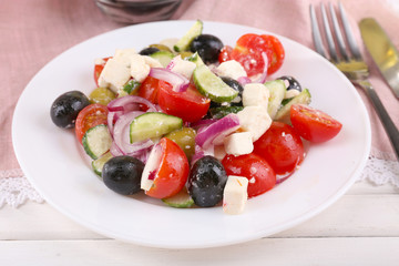 Greek salad served in plate on napkin on wooden background