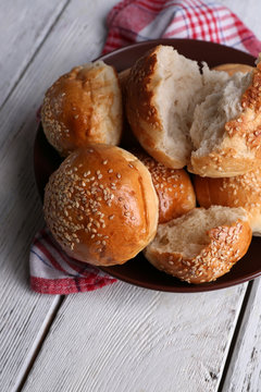Tasty buns with sesame on plate, on color wooden background