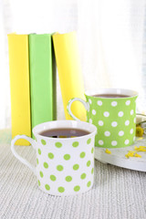Two cups of tea and books on table on curtain background